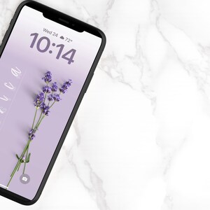 Op de afbeelding: Een smartphone met een paarse achtergrond en een takje lavendel op het scherm. De tijd is 10:14 en de datum is Wo 24. De temperatuur is 72 graden.