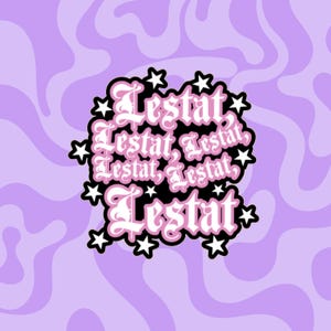 May include: A sticker featuring the name Lestat repeated multiple times in a stylized, gothic-inspired white font with a light pink outline. The text is arranged in a cluster surrounded by several small, solid white five-pointed stars on a black background.