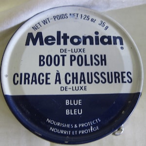 May include: A white tin can with blue lettering. The can is labeled "Meltonian De-Luxe Boot Polish" and "Cirage à Chaussures De-Luxe". The can also says "Blue Bleu" and "Nourishes & Protects Nourrit et Protège".