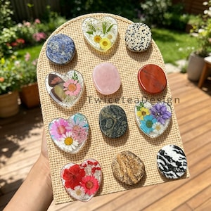 May include: A selection of resin-encased stones and heart-shaped items featuring floral and natural elements. The display includes a range of colours and textures, such as blue, pink, red, and black and white patterns. The text "Twiceteadesign" is visible.