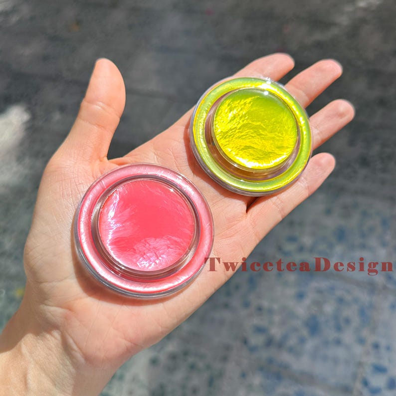 Może przedstawiać: Dwa okrągłe, przezroczyste pojemniki z kolorową zawartością trzymane w dłoni. Jeden pojemnik ma r&oacute;żowe wnętrze, a drugi ż&oacute;łte. Pojemniki mają przezroczystą, opalizującą obw&oacute;dkę. Widoczny jest tekst "TwiceteaDesign".