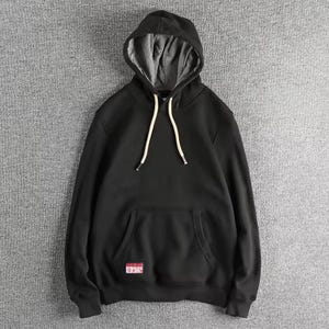 以下が含まれることがあります： グレーの裏地とフロントポケットが付いた黒いフード付きスウェットシャツ。フードには白いドローストリングと、下部に小さな赤と白のパッチが付いています。カジュアルで快適な衣服。