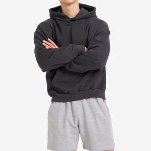 May include: A charcoal gray hoodie with a drawstring hood and a kangaroo pocket. The hoodie is paired with gray shorts. The outfit is casual and comfortable, suitable for everyday wear. The fabric appears to be a soft, medium-weight material.