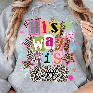 May include: A gray hoodie with a colorful graphic that reads "His Way is Better." The design features a collage of letters, stars, bows, and leopard print accents in various colors, including pink, green, and orange.