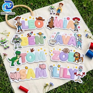 Op de afbeelding: Acht gepersonaliseerde geborduurde naamlabels met kleurrijke blokletters en diverse stripfiguren, waaronder een cowboy, space ranger, cowgirl, dinosaurus, varken en vork. Elk label toont een unieke naam: Leo, Mia, Ben, Ava, Tom, Zoe, Sam en Lily.