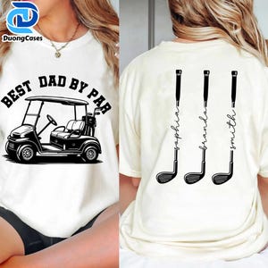 Puede incluir: Camiseta color crema con un gráfico de carrito de golf negro y el texto "BEST DAD BY PAR". La parte trasera de la camiseta presenta tres palos de golf con los nombres: Sophia, Branda y Smith.