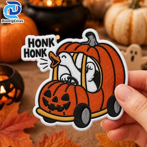 Può includere: Una toppa ricamata raffigurante un'oca bianca alla guida di un veicolo a forma di zucca arancione intagliata con un volto di lanterna. La toppa include il testo nero HONK HONK in un fumetto, con ruote nere e dettagli gialli sulla zucca.