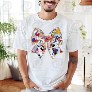 K&ouml;nnte beinhalten: Wei&szlig;es T-Shirt mit einem gro&szlig;en, bunten Schleifendesign mit Mickey Mouse und anderen Disney-Charakteren. Die Schleife ist mit roten, wei&szlig;en und blauen Sternen und Streifen verziert, die an die deutsche Flagge erinnern.