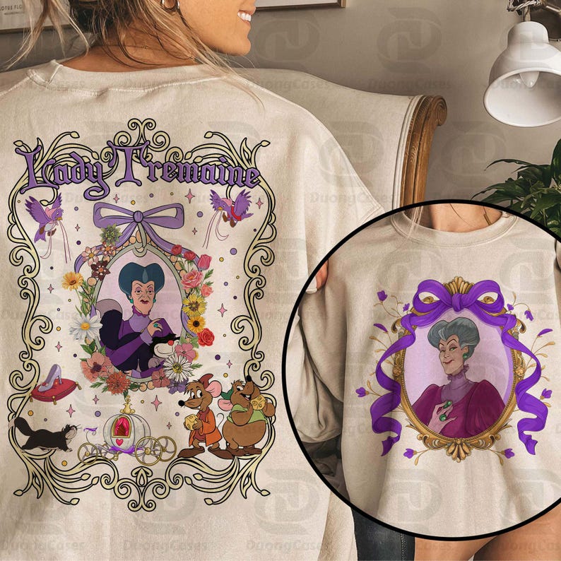 Puede incluir: Sudadera beige con un retrato enmarcado de Lady Tremaine de Cenicienta, rodeado de elementos florales y decorativos. El dise&ntilde;o incluye el texto "Lady Tremaine" en una fuente morada adornada. La sudadera tiene cuello redondo.