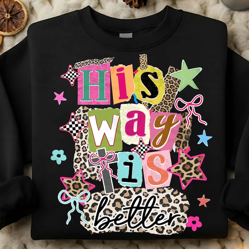 May include: Black sweatshirt with the phrase "His way is better" in a colorful, patchwork design. The design includes stars, bows, and leopard print accents, creating a vibrant and eye-catching graphic.