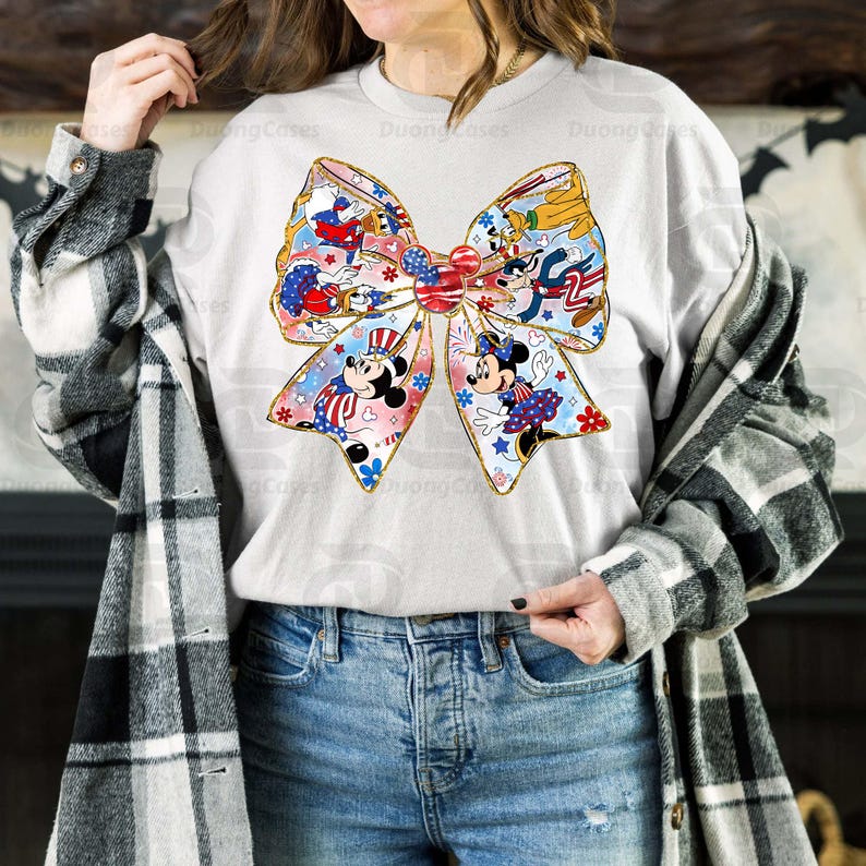 K&ouml;nnte beinhalten: Ein wei&szlig;es Langarmshirt mit einer rot-wei&szlig;-blauen Schleife mit Mickey Mouse und anderen Disney-Charakteren. Die Schleife ist mit Sternen und Streifen verziert.
