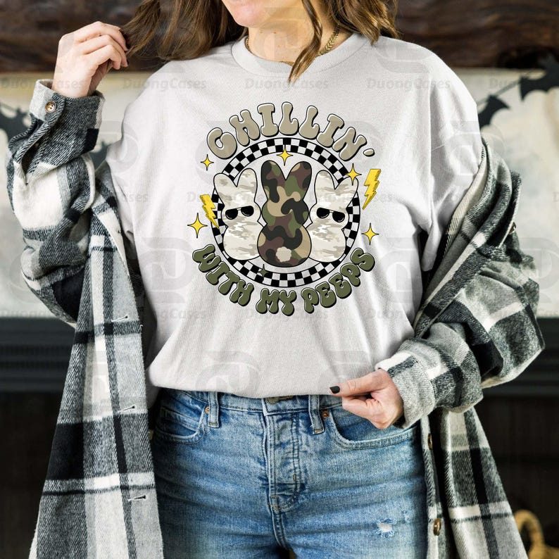 May include: A light gray sweatshirt with a graphic that says "Chillin' With My Peeps." The graphic features three cartoon bunnies wearing sunglasses, with one in camouflage. The design is surrounded by a black and white checkered circle, lightning bolts, and stars.