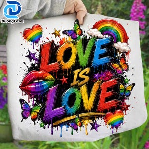 May include: A white fabric surface featuring a colorful graphic print with the text LOVE IS LOVE. The design includes rainbow-colored lips, hearts, butterflies, stars, clouds, and a rainbow arch, all rendered in a vibrant, paint-splatter style.