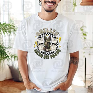 May include: White t-shirt with a graphic featuring three cartoon bunnies, one in camouflage, and the text "CHILLIN' WITH MY PEEPS" in a circular design. The design includes lightning bolts and stars.