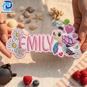 May include: A custom embroidered patch featuring the name EMILY in pink letters, decorated with white daisy flowers, a purple and blue sea turtle, and small pink hearts. The patch has a scalloped white border and a detailed stitched design.