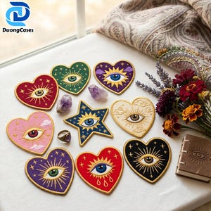 May include: A collection of embroidered fabric patches in heart and star shapes, each featuring a central eye design with radiating sunburst lines and stars. The patches come in various colors including red, green, purple, pink, black, and cream.