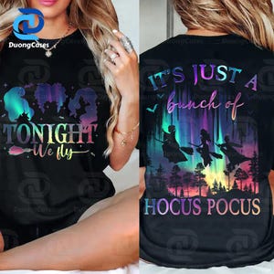 May include: Black t-shirt with a colourful graphic featuring witch silhouettes and the text "TONIGHT We fly" on the front. The back of the shirt displays the text "IT'S JUST A bunch of HOCUS POCUS" with witch silhouettes flying over a forest.