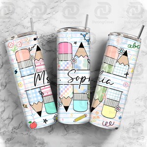 May include: Three personalized tumblers with a school theme. Each tumbler features a pencil and eraser design, with the name "Sophia" and "Ms." written on them. The tumblers are decorated with flowers, stars, and other school-related graphics.