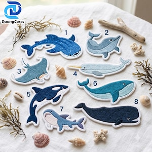 May include: A collection of eight embroidered fabric patches featuring various sea creatures, including a whale shark, dolphin, manta ray, narwhal, orca, blue whale, shark, and sperm whale, each labeled with a black number from one to eight.