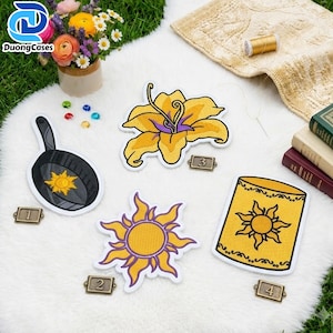 Könnte beinhalten: Vier gestickte Aufnäher, bestehend aus einer schwarzen Pfanne mit Sonnensymbol, einer gelben Lilie, einer gelben strahlenden Sonne und einer gelben Laterne mit Sonnenmotiv. Jeder Aufnäher ist mit einer kleinen Metallnummer von eins bis vier versehen.