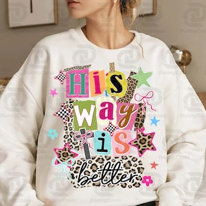 May include: White sweatshirt with the text "His way is better" in a colorful, patchwork design. The design includes stars, bows, and leopard print accents, creating a vibrant and eye-catching graphic.