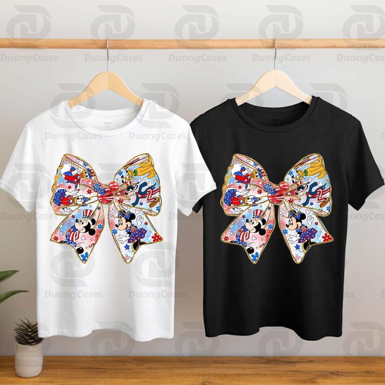 K&ouml;nnte beinhalten: Zwei T-Shirts mit einem gro&szlig;en Schleifendesign. Die Schleife besteht aus einem bunten Muster mit Mickey Mouse und Minnie Mouse Figuren. Ein Shirt ist wei&szlig; und das andere ist schwarz.