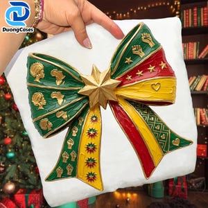 May include: A decorative bow with green, red, and yellow accents, featuring gold stars, fists, and African continent shapes. The bow is centered with a gold star and is held against a white background.