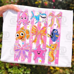 May include: White fabric featuring colorful cartoon sea creatures and bows on pink striped background. Includes an octopus, shark, clownfish, Dory, starfish, and seahorse. The design is playful and vibrant.