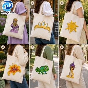 May include: A collection of six off-white canvas tote bags, each featuring a distinct embroidered design: a person with long blonde hair, a gold tiara, a yellow sun, a yellow flower, a green chameleon, and a tall stone tower with long hair.