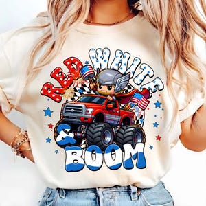 Puede incluir: Sudadera de color crema con un dise&ntilde;o gr&aacute;fico que presenta un cami&oacute;n monstruo rojo conducido por un personaje de dibujos animados. El dise&ntilde;o incluye las palabras "Red, White & Boom" en rojo, blanco y azul, con estrellas y banderas. El cami&oacute;n tiene neum&aacute;ticos negros grandes.