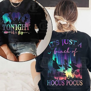 May include: Black sweatshirt with the text "TONIGHT We fly" and silhouettes of three figures. The back of the sweatshirt features the text "IT'S JUST A bunch of HOCUS POCUS" with silhouettes of witches flying over a forest.