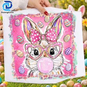 May include: White Easter-themed graphic featuring a bunny wearing heart-shaped glasses and a pink polka-dot bow, blowing a bubblegum bubble. The design includes colorful Easter eggs and a pink background with a leopard print border. The image is on a white surface.