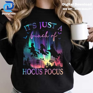 May include: Black sweatshirt with a colorful graphic featuring three witch silhouettes flying on broomsticks against a vibrant aurora background. The text "IT'S JUST A bunch of HOCUS POCUS" is displayed in a gradient font.