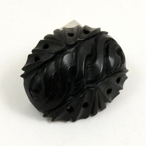May include: A black carved oval-shaped button with intricate designs and holes.