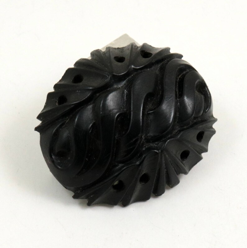 May include: A black carved oval-shaped button with intricate designs and holes.
