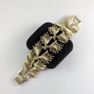 May include: A gold-tone bracelet featuring a delicate, intricate design of stylised leaves. The bracelet is made of metal and has a clasp fastening.