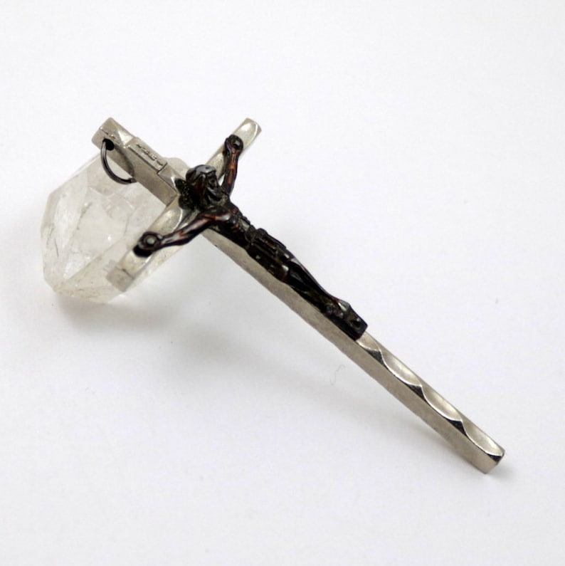Puede incluir: Un colgante de cruz de plata con una figura de Jes&uacute;s marr&oacute;n oscuro. La cruz tiene un dise&ntilde;o texturizado en la parte posterior.