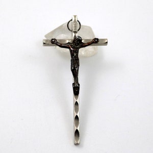 Puede incluir: Un colgante de cruz de plata con una figura de Jes&uacute;s de color marr&oacute;n oscuro. La cruz tiene un dise&ntilde;o texturizado.
