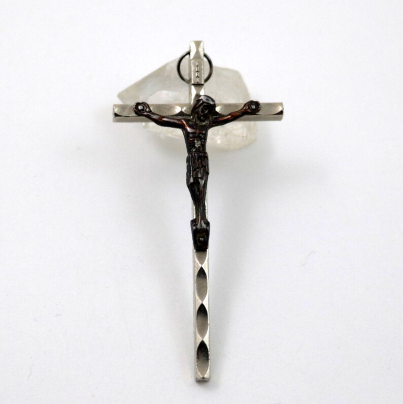 Puede incluir: Un colgante de cruz de plata con una figura de Jes&uacute;s de color marr&oacute;n oscuro. La cruz tiene un dise&ntilde;o texturizado.