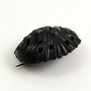 May include: A black carved jet brooch with an intricate design. The brooch has a pin on the back for attaching to clothing.