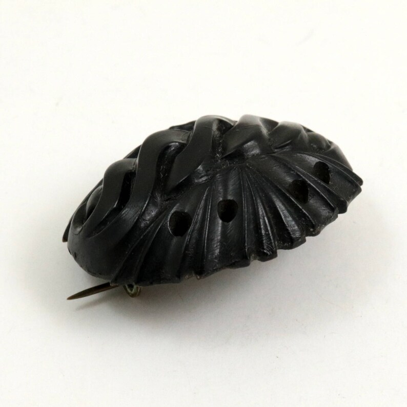 May include: A black carved jet brooch with an intricate design. The brooch has a pin on the back for attaching to clothing.