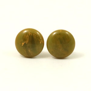 May include: A pair of green and gold marbled plastic earrings. The earrings are round and have a smooth, glossy finish.