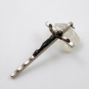 Puede incluir: Colgante de cruz de plata con una figura de Jes&uacute;s marr&oacute;n oscuro. La cruz tiene un dise&ntilde;o texturizado y retorcido.