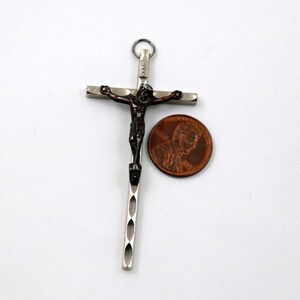 Puede incluir: Un colgante de cruz de plata y bronce con una figura detallada de Jesucristo. El colgante se muestra junto a un centavo estadounidense para comparar el tama&ntilde;o.