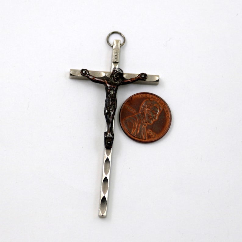 Puede incluir: Un colgante de cruz de plata y bronce con una figura detallada de Jesucristo. El colgante se muestra junto a un centavo estadounidense para comparar el tama&ntilde;o.