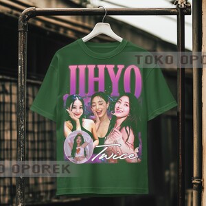 Puede incluir: Camiseta verde con un dise&ntilde;o gr&aacute;fico retro de tres mujeres y la palabra "Twice". La camiseta tambi&eacute;n presenta el nombre "IHYO" en rosa. La camiseta est&aacute; colgada en un perchero de metal.