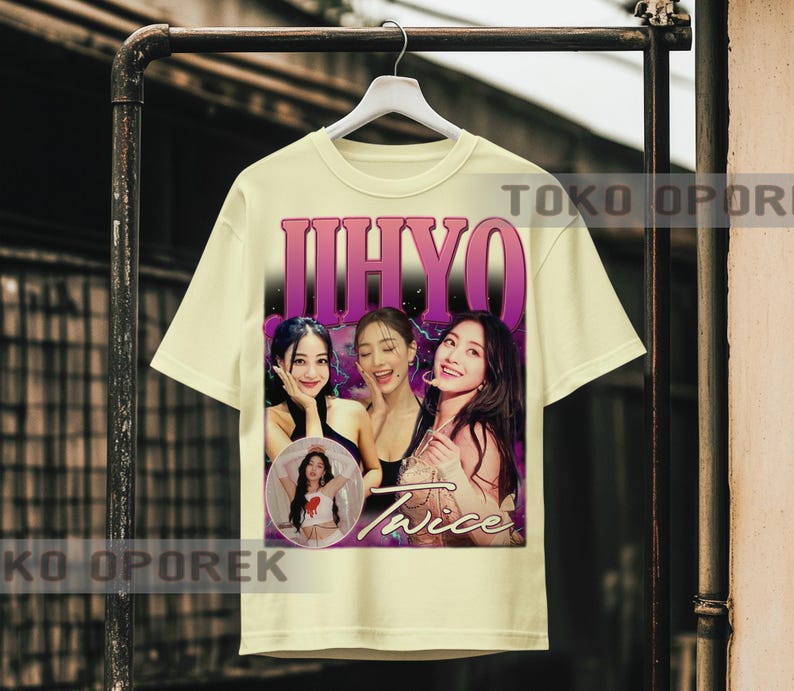 Puede incluir: Camiseta color crema con un gr&aacute;fico de tres mujeres y la palabra "JIHYO" en una fuente degradada p&uacute;rpura. La palabra "Twice" tambi&eacute;n es visible. La camiseta est&aacute; colgada en un estante de metal.