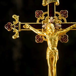 K&ouml;nnte beinhalten: Vergoldetes Kreuz mit detaillierter Jesusfigur. Das Kreuz hat burgunderfarbene Akzente und dekorative florale Elemente. Die Inschrift "INRI" ist auf einem Banner &uuml;ber der Figur zu sehen.