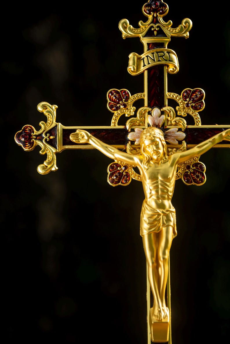 K&ouml;nnte beinhalten: Vergoldetes Kreuz mit detaillierter Jesusfigur. Das Kreuz hat burgunderfarbene Akzente und dekorative florale Elemente. Die Inschrift "INRI" ist auf einem Banner &uuml;ber der Figur zu sehen.