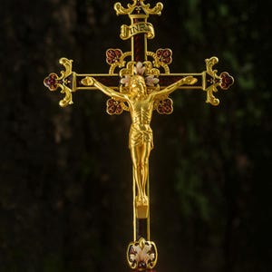 K&ouml;nnte beinhalten: Ein goldfarbenes Kruzifix mit einer detaillierten Figur Jesu Christi. Das Kreuz weist aufwendige Details mit roten und goldenen Akzenten auf. Der Sockel hat eine passende rot-goldene Farbe, und das Kreuz tr&auml;gt oben die Buchstaben INRI.